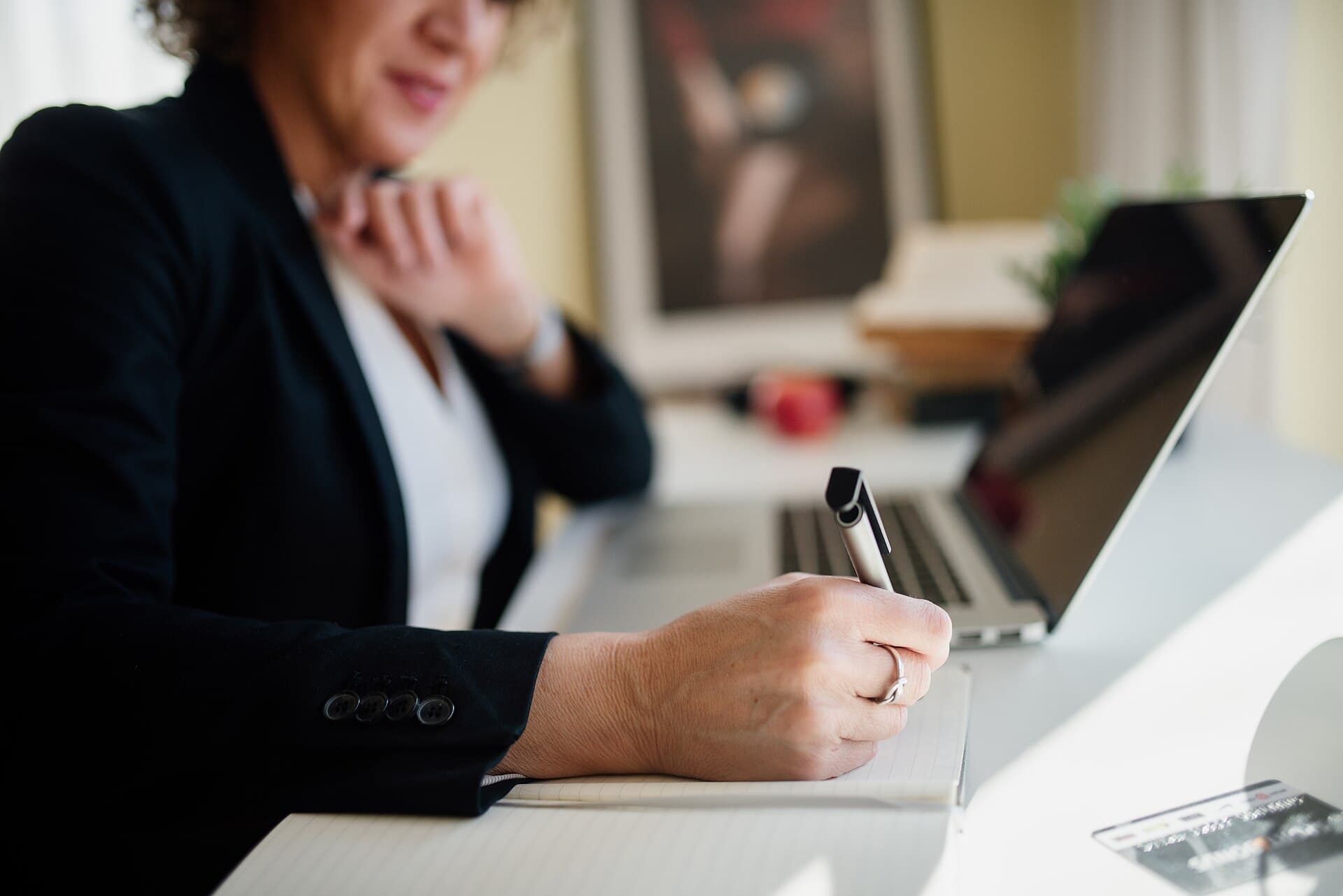 A business owner making notes on a notepad next to an open laptop, planning next steps